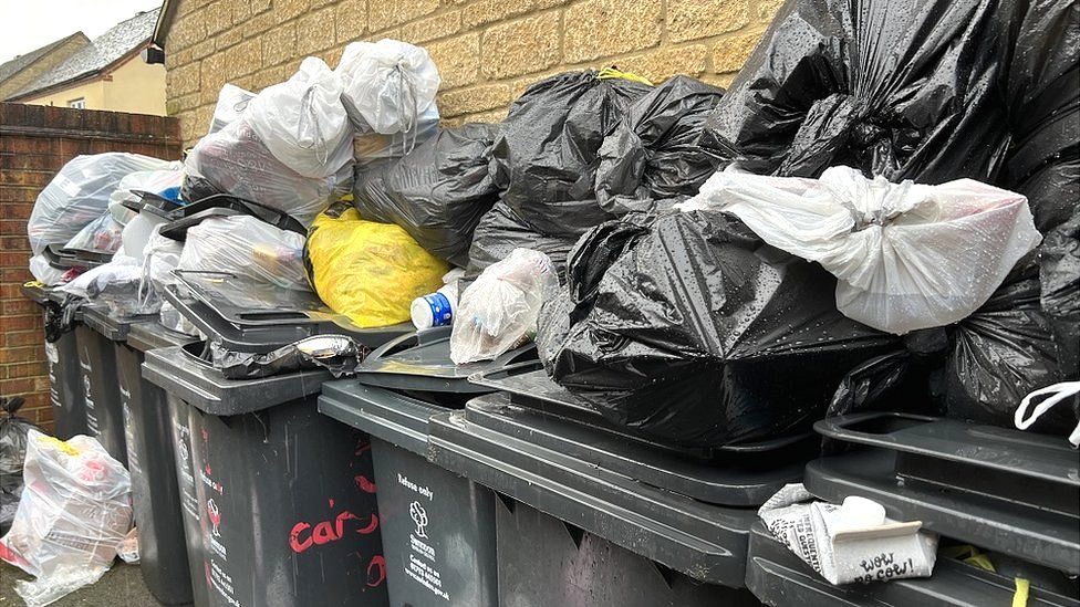 A row of bins in a bin store full with full bin bags balanced on top