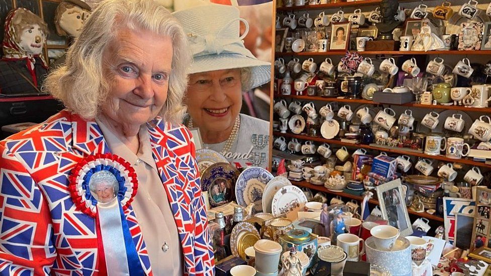 Margaret Tyler wearing a union flag jacket surrounding by her collection of royal memorabilia