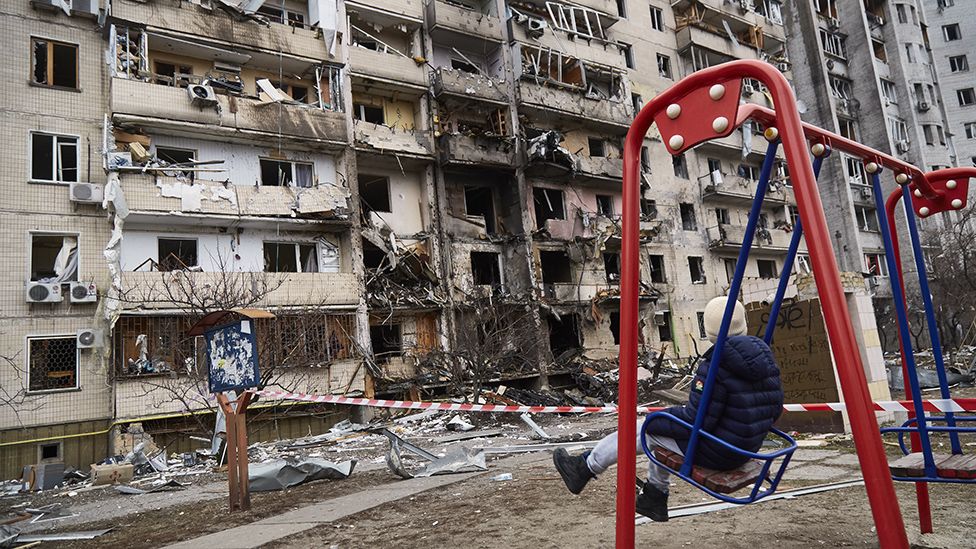 A child on a swing outside a residential building damaged by a missile on February 25, 2022 in Kyiv, Ukraine.