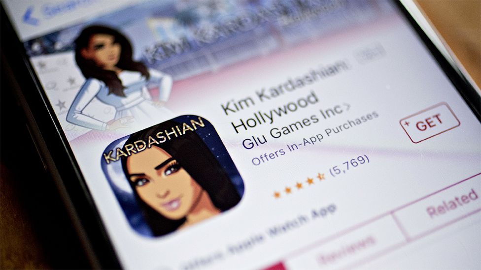 Kim Kardashian: Hollywood game is seen in the App Store on an Apple iPhone, with black outer screen and an animated image of Kim Kardashian with black hair, on the screen.