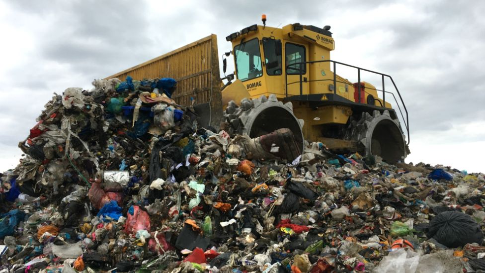 Landfill compactor vehicle on top of large pile of landfill