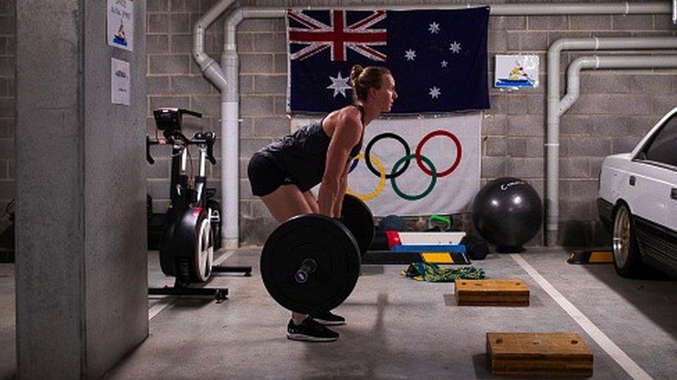 Jo lifting weights in a makeshfit gym in a garage