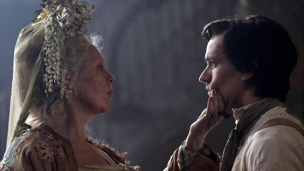 Olivia Colman as Miss Havisham holding Fionn's head in her hand, they are looking into each other's eyes