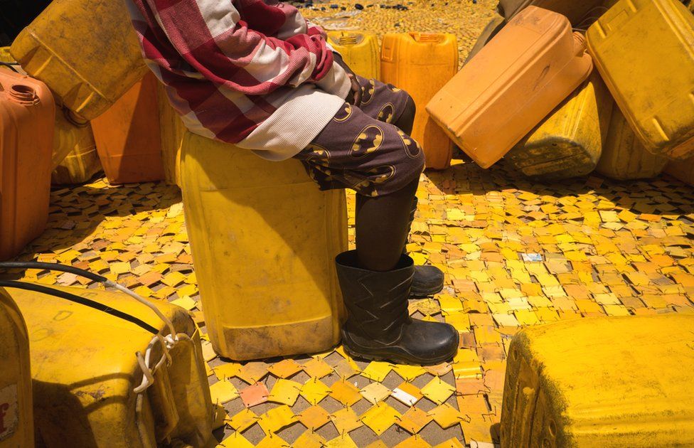 Someone sitting on a jerry can on some yellow tapestry created by artist Serge Attukwei Clottey on a road in La - Accra, Ghana