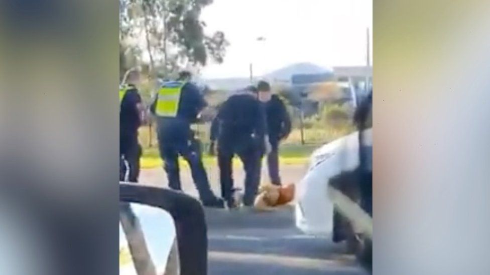 Four police officers stand over the man who is lying on the ground during the arrest