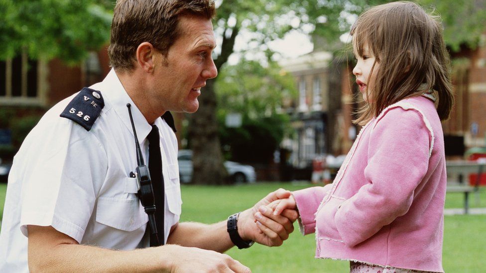 Policeman crouching to talk girl (3-5), outdoors, side view