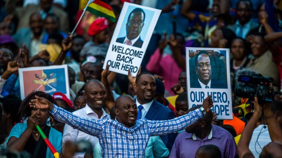 Supporters hold banner, wave Zimbabwean national flag and cheer as they gather to welcome Zimbabwe"s incoming President Emmerson Mnangagwa upon his arrival at Zimbabwe"s ruling Zanu-PF party headquarters in Harare on November 22, 2017.