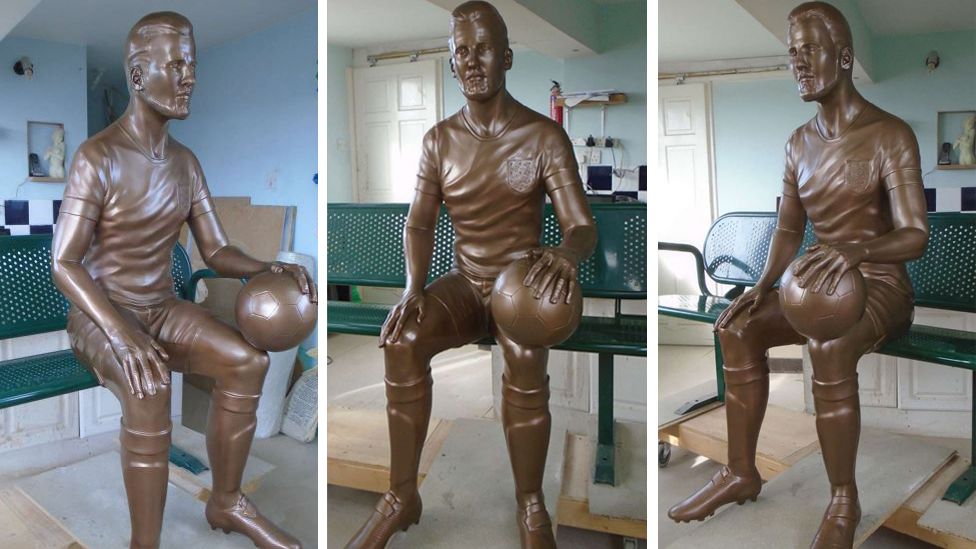 The statue of Harry Kane shows the footballer sat on a green bench with a football on his knee
