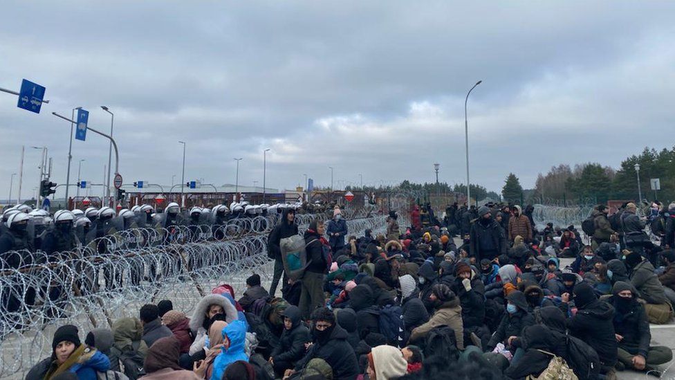 Migrants wait at a border crossing as Polish troops watch on