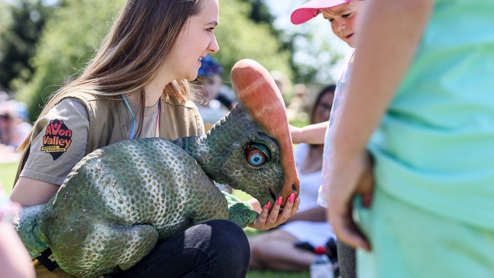 A woman holds a toy dinosaur at Avon Valley country park while a child looks on