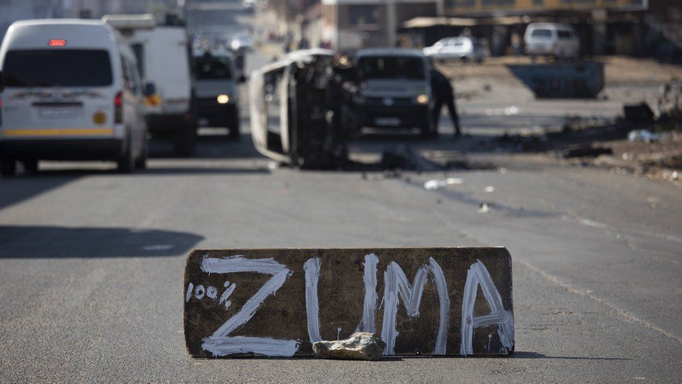 A burned car is seen at a road block during ongoing violent clashes in downtown Johannesburg, South Africa, 11 July 2021