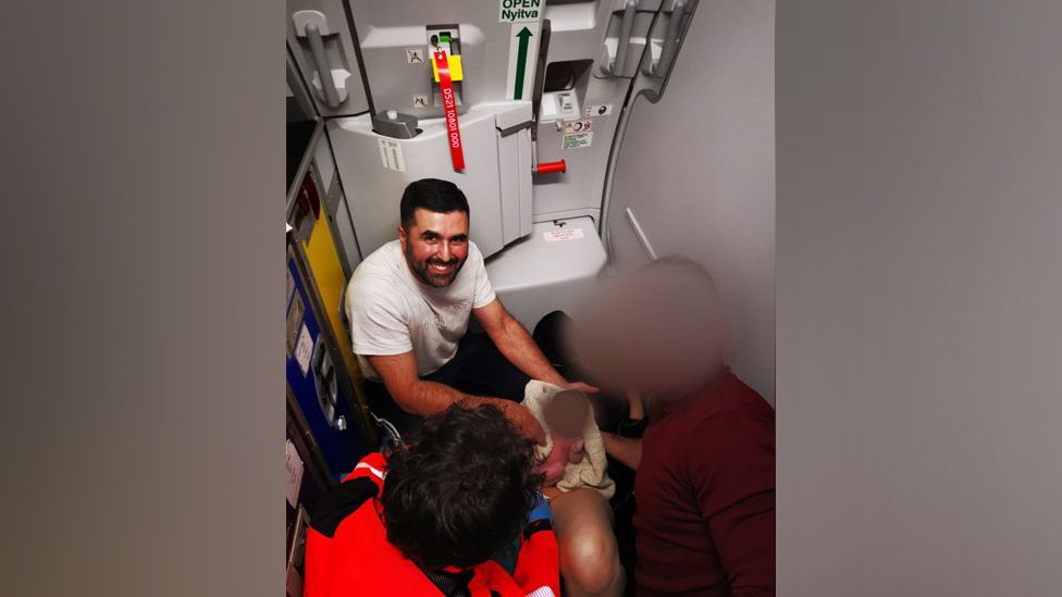 Hassan Khan poses with the baby and her mother, both who have been blurred, on the plane