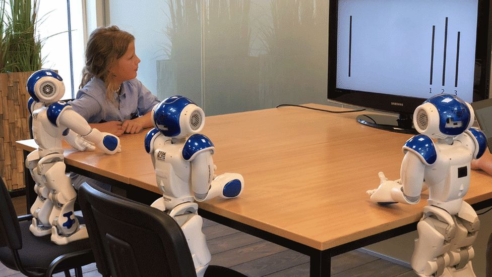 Girl looks at screen with three Nao robots