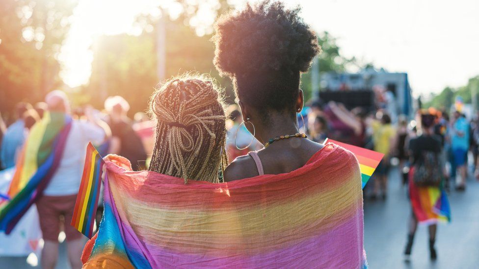 Young female couple hugging with rainbow scarf at pride event