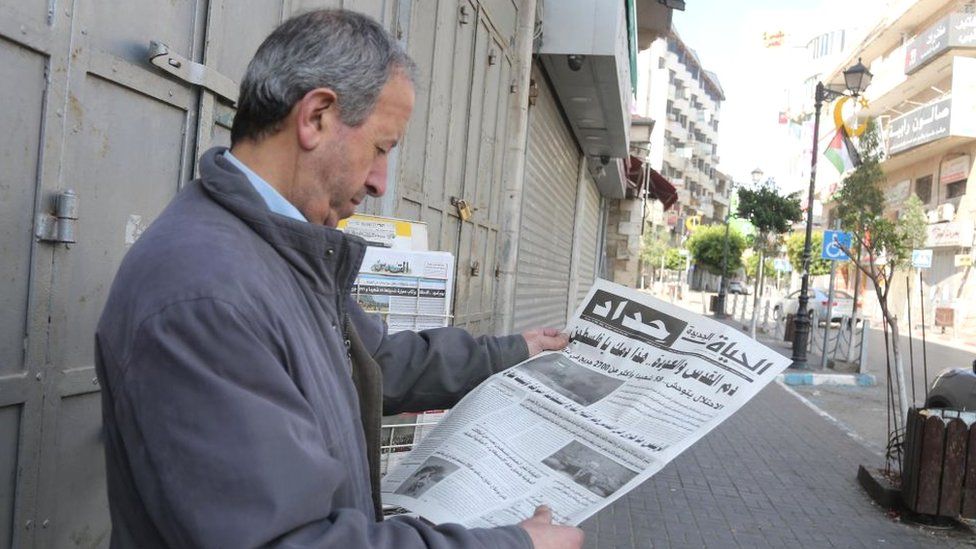 A man reads a newspaper in front of closed shops in Ramallah