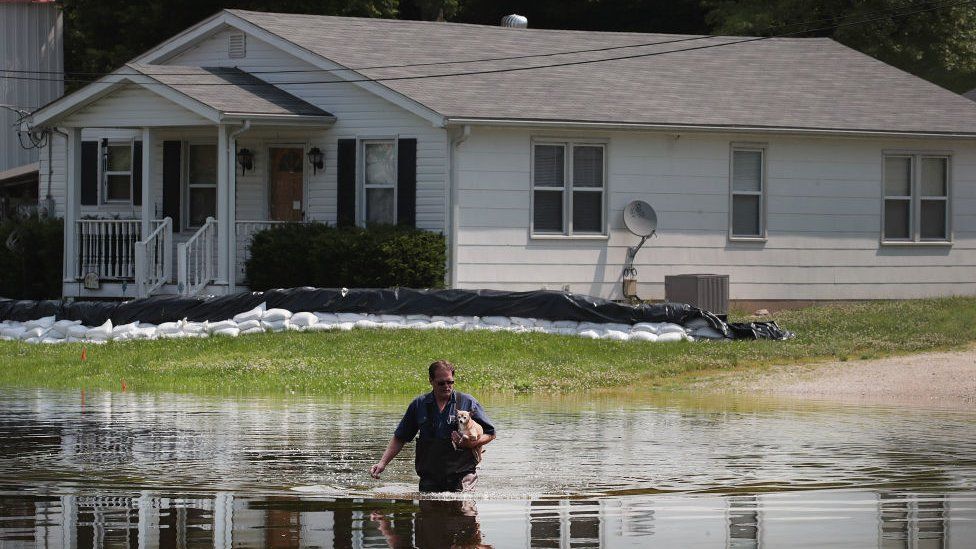 A man walks through floodwater from the the Mississippi River as he leaves his home with his dog Tiny