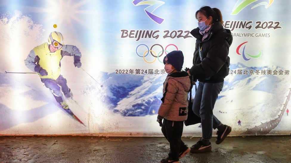 Женщина и ребенок проходят мимо плаката зимних Олимпийских игр в Пекине