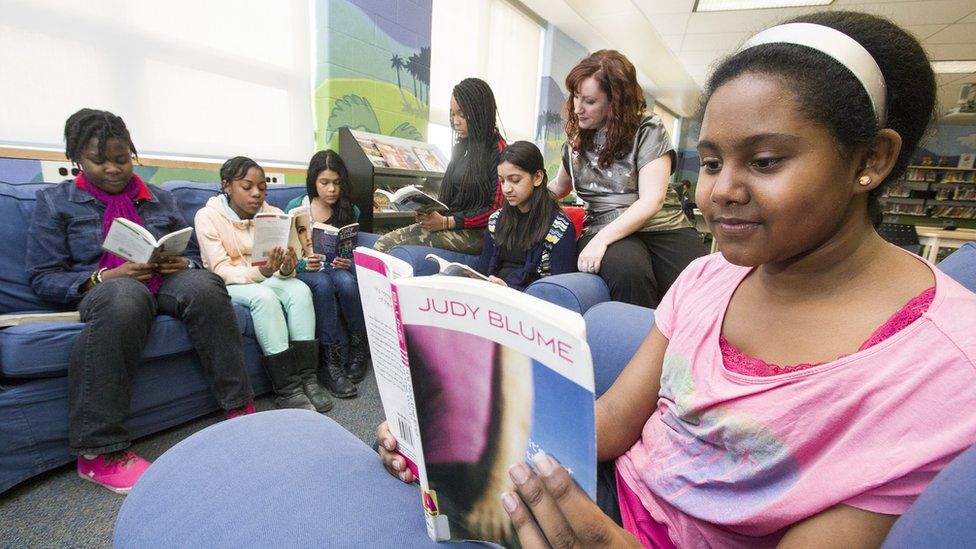 A girl reading a Judy Blume book with other girls reading in the background