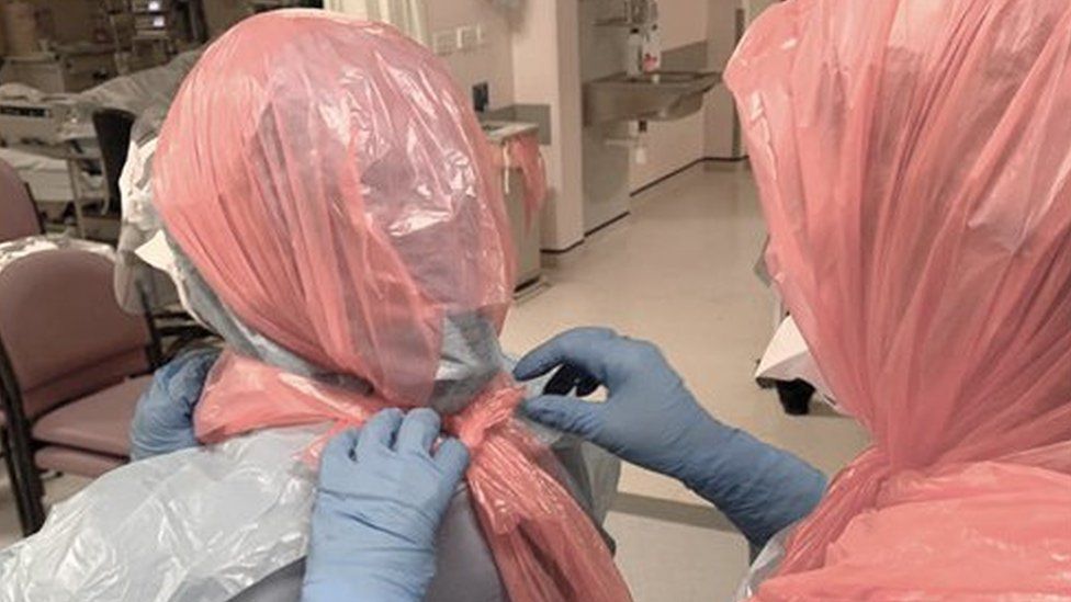 A doctor helping her colleagues by securing bin bags over their heads