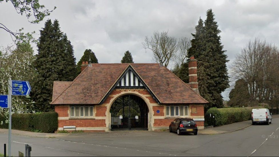 Single-storey brick building with archway entrance. There are tall trees on either side