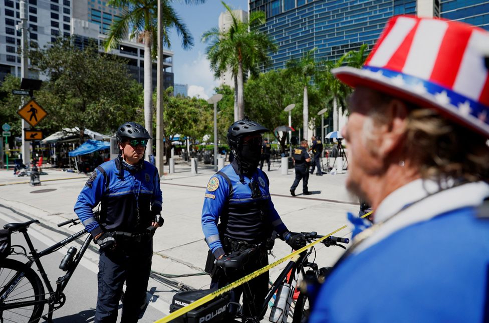 Полицейские стоят на улице, оцепленной лентой, после того, как на ней была обнаружена оставленная без присмотра посылка, возле здания суда США Уилки Д. Фергюсона-младшего в день, когда бывший президент США Дональд Трамп должен явиться по обвинению в секретных документах в Майами. , Флорида