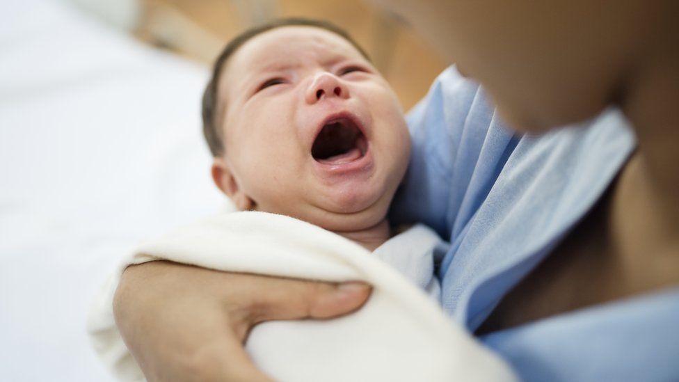 newborn baby crying in mother's arms