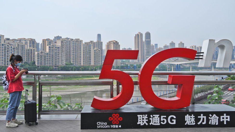 Женщина стоит рядом со знаком China Unicom 5G в Чунцине, Китай.