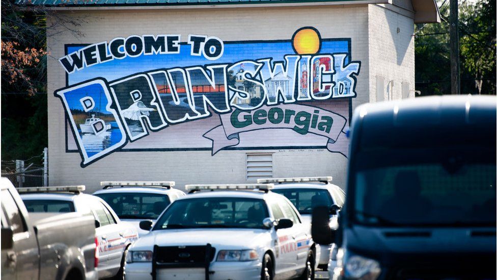 Mural saying Welcome to Brunswick Georgia with police cars in front