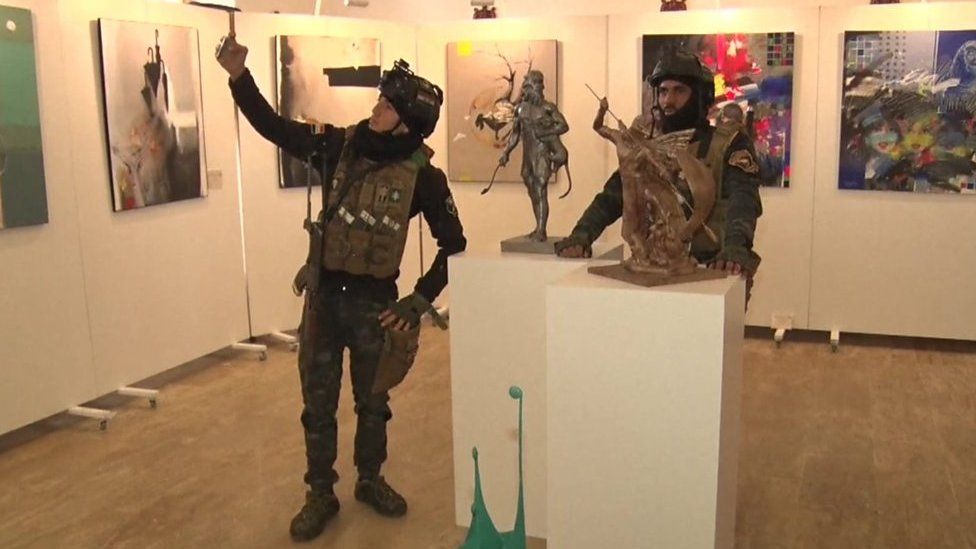 Two Iraqi soldiers, including one taking a selfie next to a sculpture