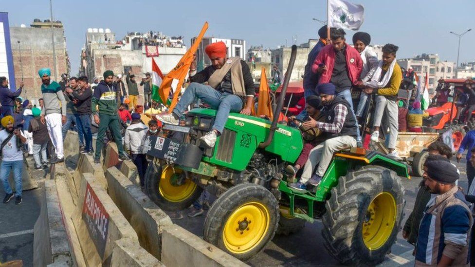 Farmers run a tractor over a barricade at the Delhi- Ghazipur border.