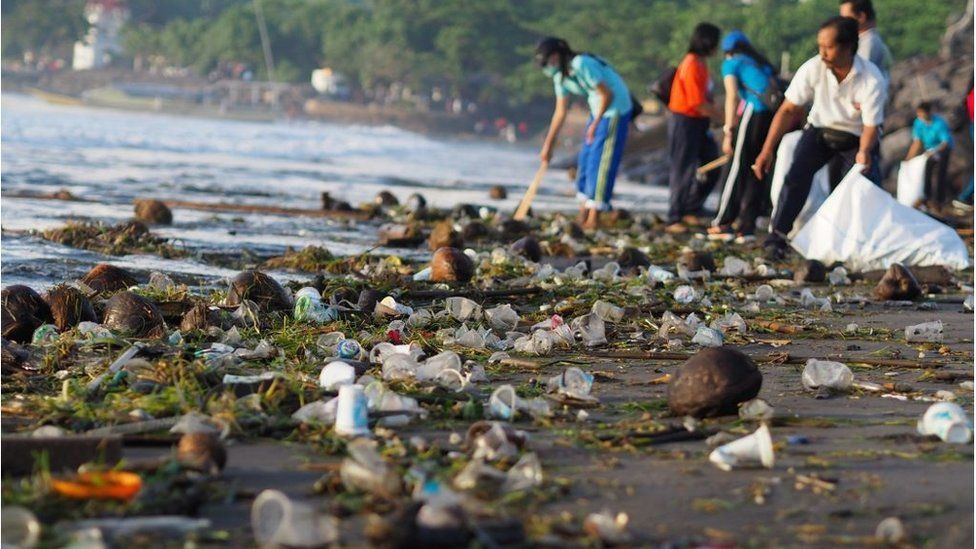 People and children work together cleaning up Sanur Beach from plastics and woods waste in Bali on April 13, 2018