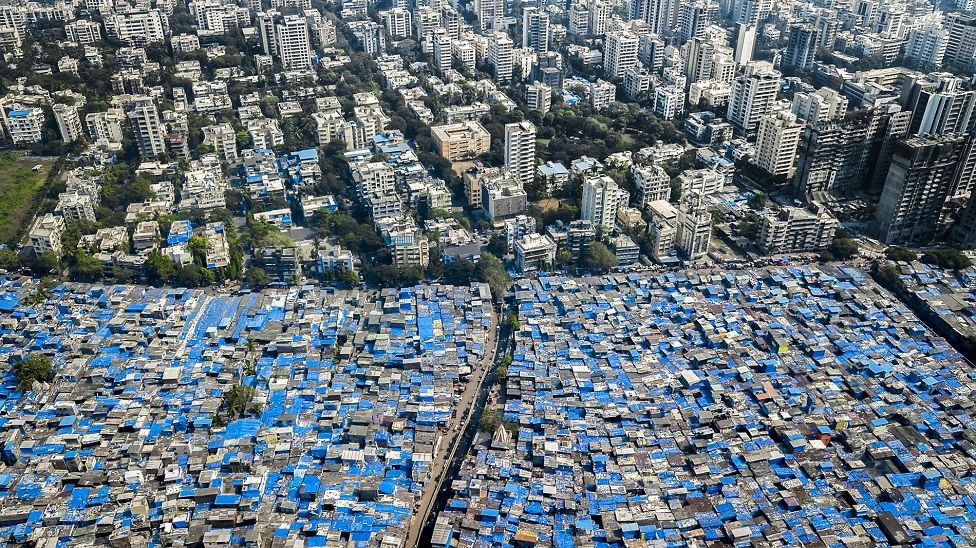 Prédios de um lado e casas com telhaod de lona azul para proteger das chuvas, em Mumbai, Índia