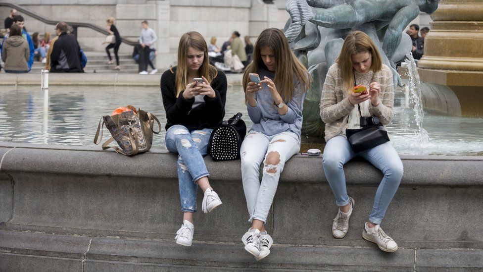 Teenage girls on smartphones in Trafalgar Square.