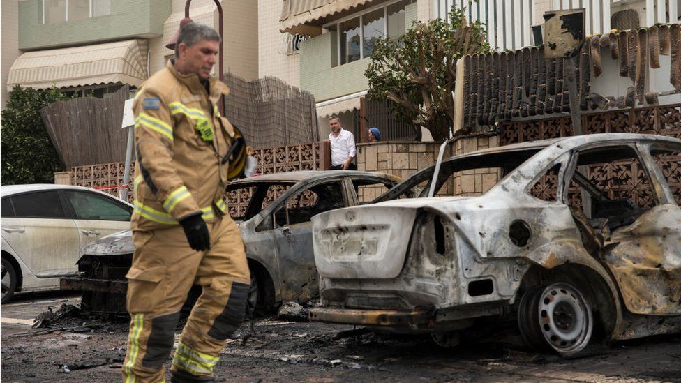 Израильский пожарный идет по сгоревшим автомобилям после того, как ракета, выпущенная из сектора Газа, попала в Ашдод