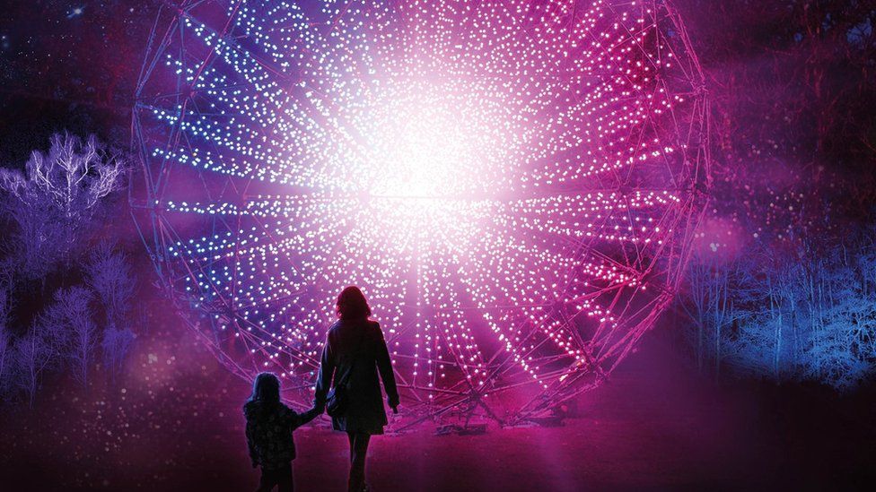 Silhouette of a woman and a small child in front of a circular light installation of hundreds of small lights