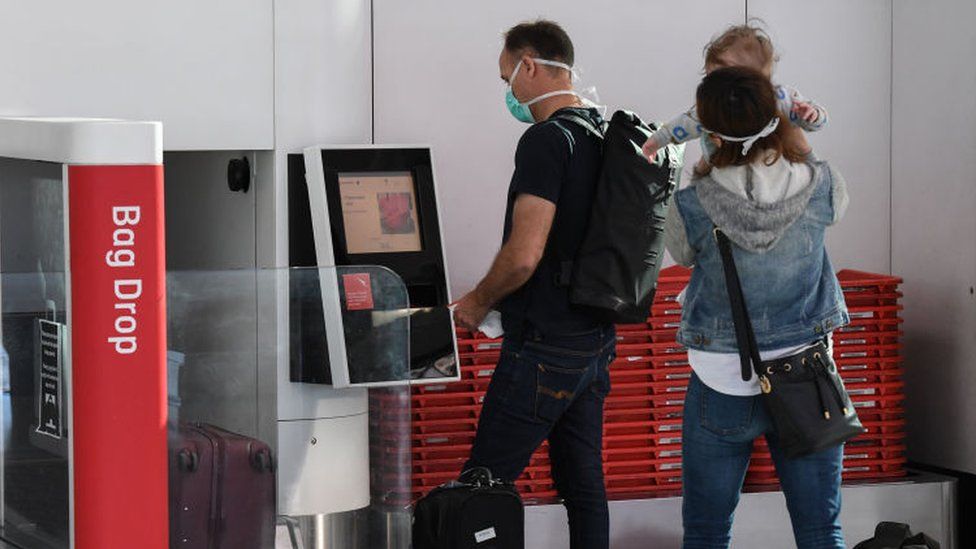 Passengers wearing face masks use a check in machine at Sydney airport