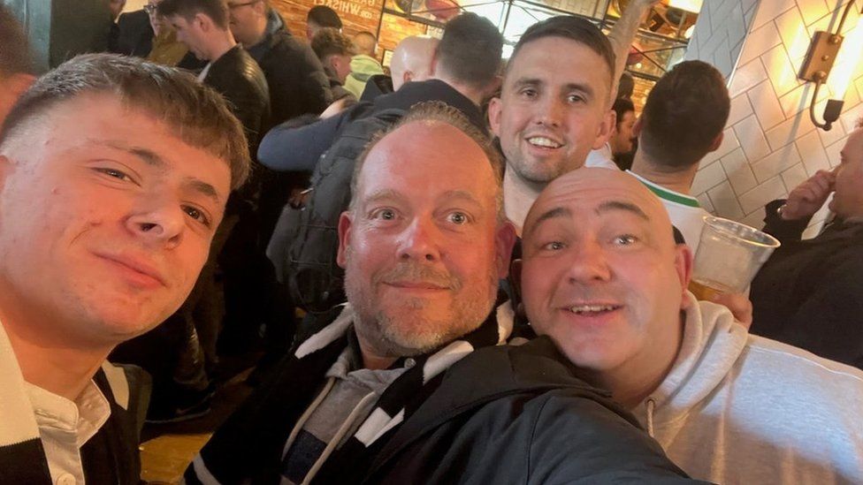 Four men smile at the camera in a selfie