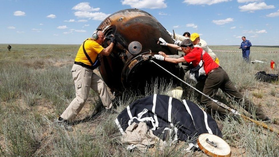 Search and rescue team members roll the Soyuz capsule over