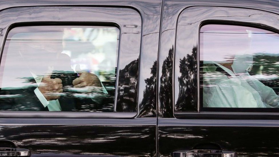 President Donald Trump gives two thumbs up to supporters as he rides in the presidential SUV with two Secret Service agents wearing medical protective masks, goggles and protective gowns