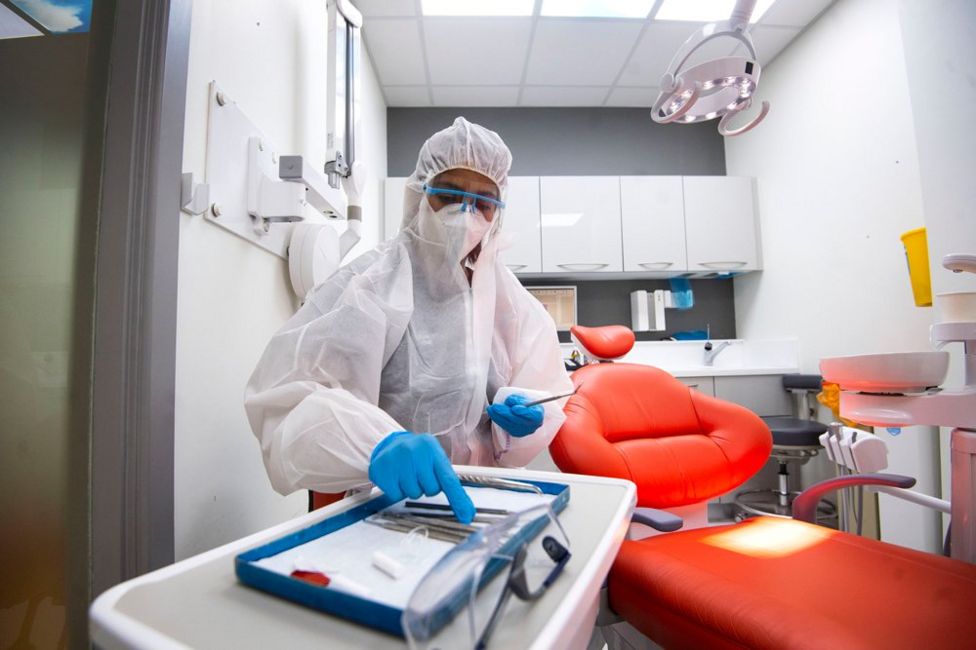 A dentist in full PPE arranges dental equipment inside their practice