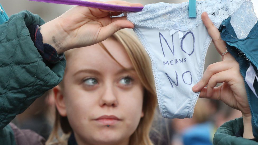 A young woman holds up white women's underwear with the words "No means no" written upon them at the Dublin protest
