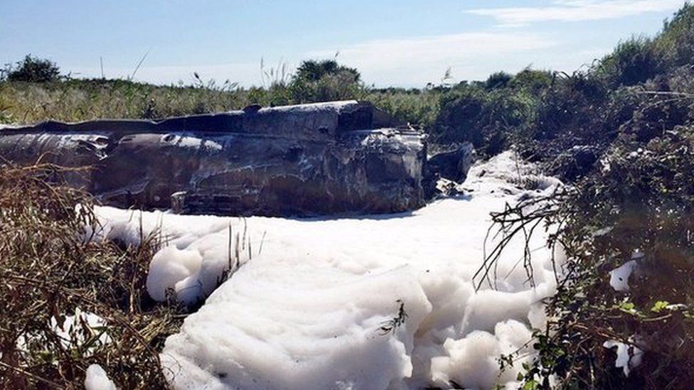 Foam surrounds the burnt-out fuselage of the Hawker Hunter jet