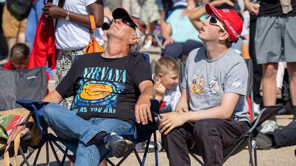 One young man and one old man, both in casual clothing, look skywards in sunglasses in caps