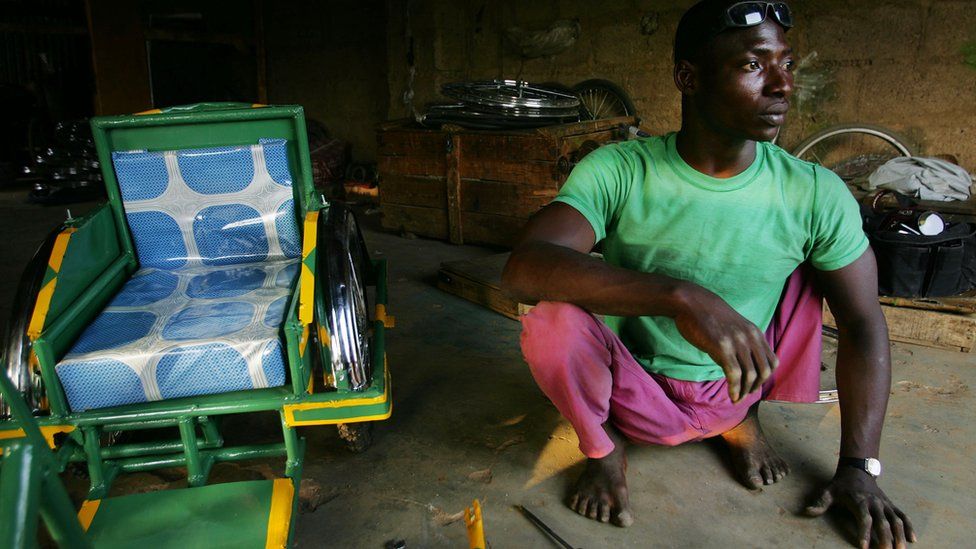 Polio sufferer Rabiu Lawal sits on his emaciated legs next to a hand-cranked tricycle he's assembling at the Polio Victims Association April 7, 2005 in Kano, Nigeria.