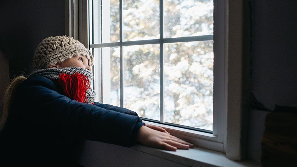 Девушка смотрит в окно в холодный день