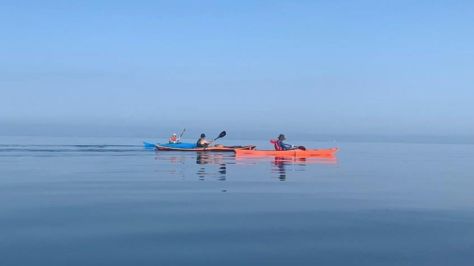Three people in kayaks on the sea