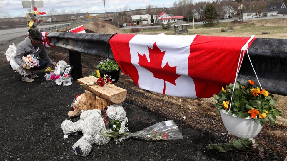 A woman adjusts flowers at a makeshift roadside memorial for Royal Canadian Mounted Police Constable Heidi Stevenson