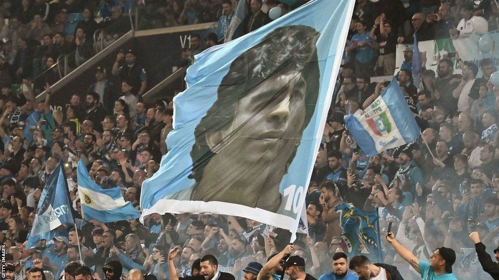 A flag with Diego Maradona's face on it is waved by Napoli fans