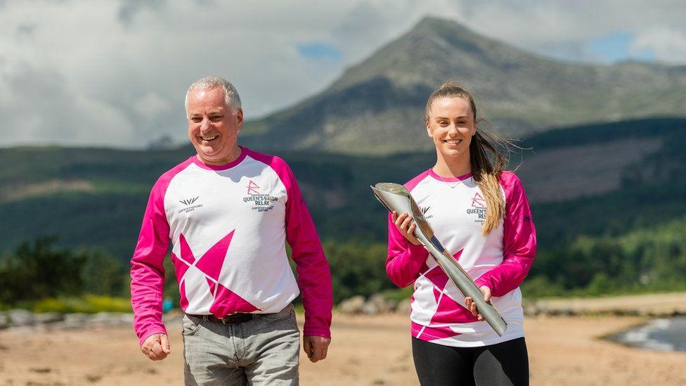 Former Scottish First Minister Jack McConnell, now Lord McConnell, hands the baton to badminton player Eleanor O'Donnell on Brodick beach