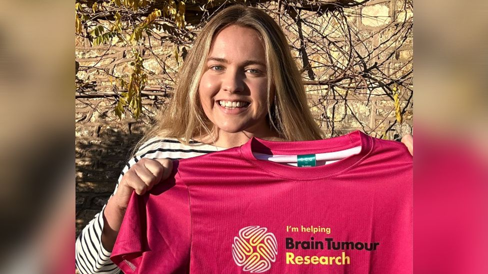 Megan smiling whilst holding up a pink t-shirt saying 'Brain Tumour Research'